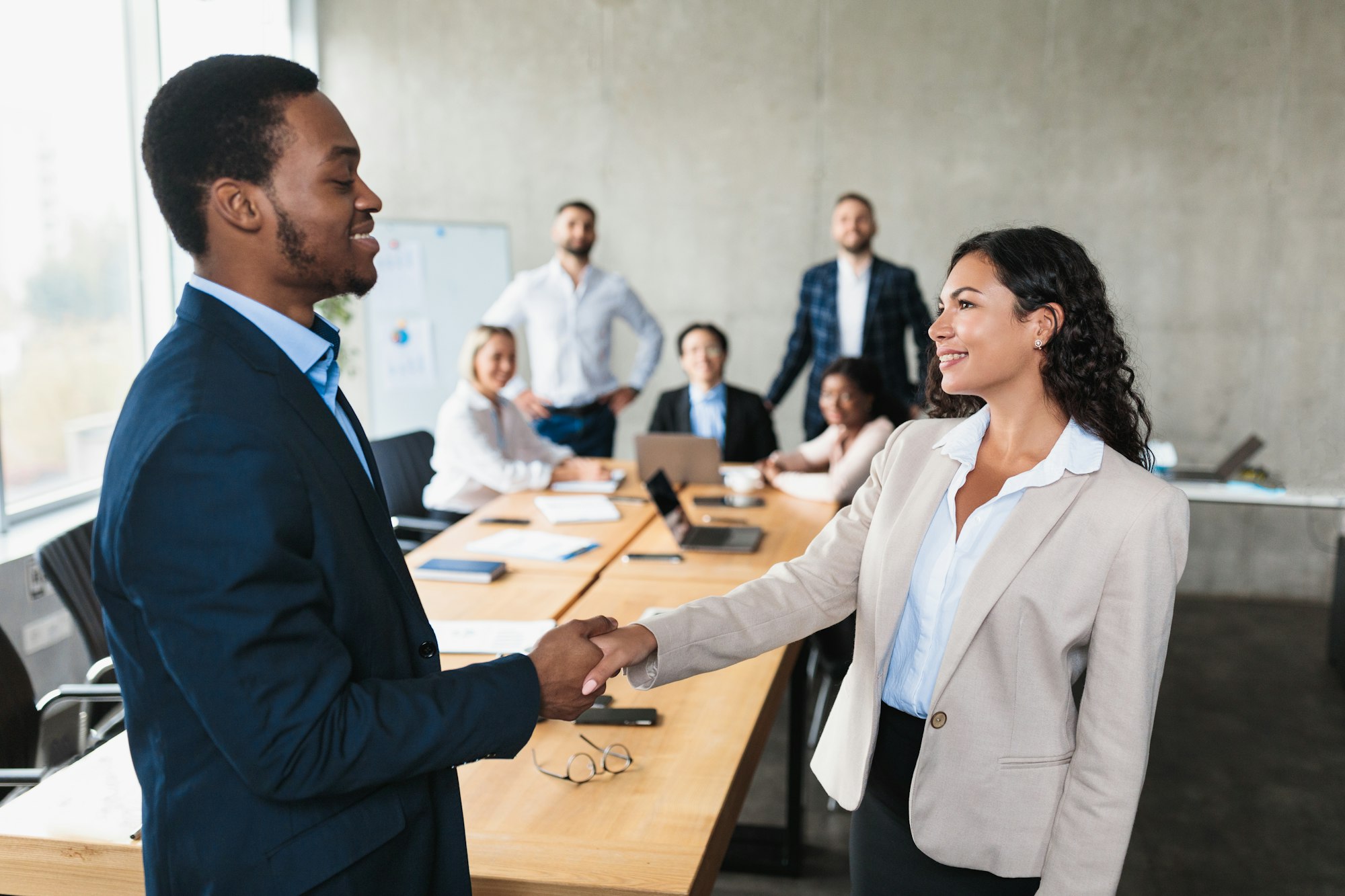 African Businessman And Latin Businesswoman Shaking Hands In Modern Office